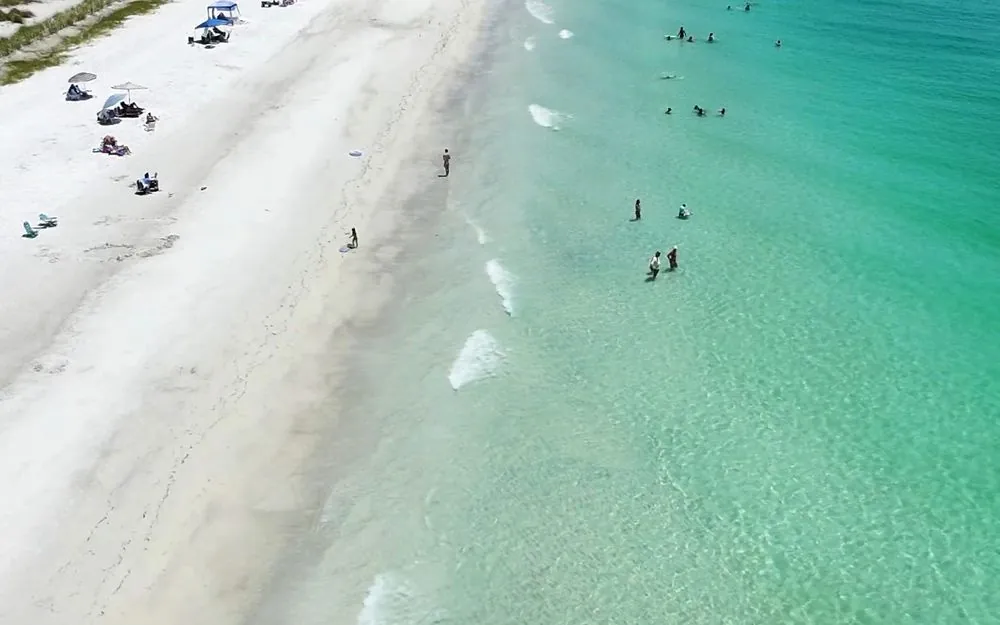 A Gulf Coast beach from above, with umbrellas on the sand and clear green water